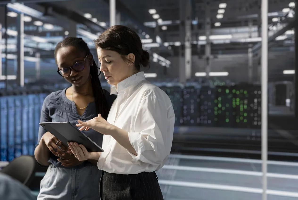 Two engineers reviewing live infrastructure dashboards on a tablet in a data centre