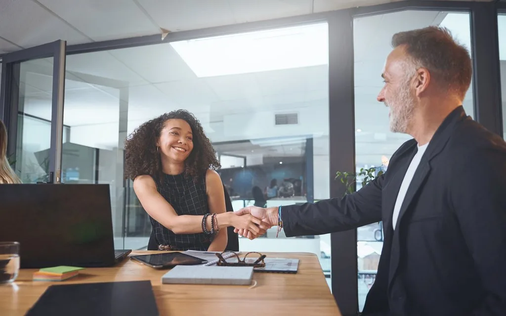 Two smiling business people shaking hands during a meeting in an office